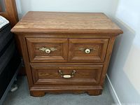 Front view of the vintage Thomasville wooden nightstand showing three drawers and decorative hardware with some wear on the wood finish.