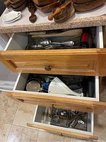 Photo showing three drawers open containing assorted kitchen utensils including cutlery, wooden spoons, and metal tools.