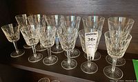 Twelve Waterford Lismore wine glasses arranged on a shelf; six red wine glasses in front row and six taller white wine glasses behind