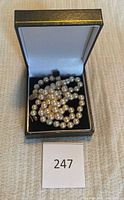 Pearl necklace coiled inside black jewelry box with lot tag ‘247’