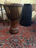 First djembe drum standing on carpet with padded carrying case in background