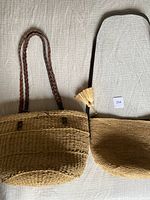Two woven jute shoulder bags laid out flat showing textures and straps, one with braided leather straps and bucket shape, the other with adjustable strap and tassel detail.