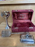 6.5 inch gold and silver tree of life Kiddush cup standing next to open red velvet presentation box and silver plated serving tongs and lid.