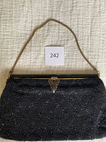 Full view of the vintage black evening clutch showing the beaded pattern, metal chain strap, and Art Deco clasp laying flat on a textured fabric surface.