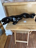 Side angle showing full length and glossy black finish of the crouching panther figurine on a wooden surface.