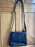 Front view of black leather Bree shoulder bag hanging against wooden background