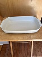 Front view of white rectangular cast iron baking dish with handles on side placed on a wooden chair.