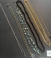 Multiple necklaces laid flat showing variety of styles including bead and chain designs in silver and gold tone finishes.