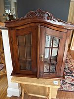 Front and side view of closed vintage wood curio cabinet showing carved top, glass paneled double doors with key lock, rich dark wood finish.