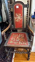 Full view of barley twist armchair with red floral needlepoint upholstery and cane back of seat.
