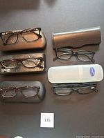 Five pairs of eyeglasses arranged with their corresponding cases on a black surface. One pair has a visible transparent reading glasses case.