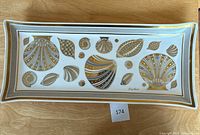 Top view of rectangular milk glass platter with gold seashell design and signature.