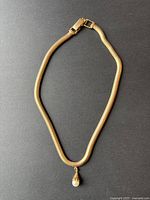 Full view of serpentine gold chain necklace laid flat on dark background showing chain and pendant