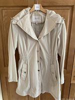 Full view of cream coloured Laundry by Shelley Segal spring trench coat with elastic waist, button flap pockets, and collar with shoulder snaps