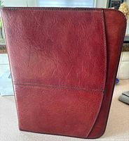 Closed bright reddish brown leather portfolio with stitch detailing