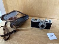 Camera with attached lens and open leather case on wooden surface