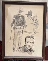 Overall view of framed lithograph showing multiple sketches of John Wayne in various poses, wood frame and glass front.