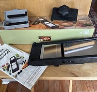 Overview of mandoline, comb attachments in case, food holder and manual on original box