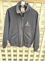 Black wool jacket with embroidered Paragon Motion Pictures logo on chest, full front zipper, pockets, and ribbed cuffs and hem.