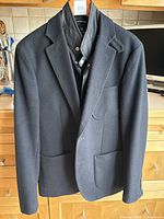 Full view of the men's black insulated jacket on a hanger showing the front with lapel collar and two lower patch pockets.