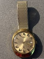 Full view of gold-tone watch and mesh bracelet on grey surface