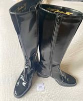 Pair of black patent leather full-length lined boots standing upright on white surface, showing overall profile and shape including 1.5 inch heels and side zippers.