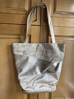 Front of gold metallic Toni Pons shoulder bag hanging showing full length straps and textured fabric details