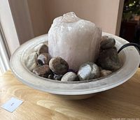 Angled close-up photo showing the central large rough rose quartz crystal surrounded by natural stones in the frosted circular bowl with power cord visible
