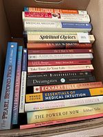 Photo of 15 self-help and novel books stacked in cardboard box showing titles and authors