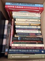 Photo showing a collection of self help and novel books stacked in a box, titles clearly visible.