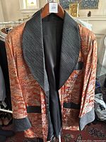 Full view of vintage men's smoking jacket showing Asian inspired pattern, black satin quilted shawl collar, sash belt, and pockets.