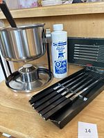 Full view of fondue pot on stand with burner and 6 forks laid out, also fondue fuel bottle