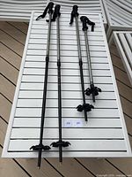 Two pairs of trekking poles displayed on white slatted surface, showing full length of poles with basket tips and pointed ends
