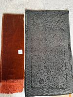 Rust colored velvet scarf next to green sheered burnout velvet shawl, both laid flat on neutral background.