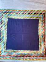 Full view of the scarf laid flat showing the multicolor striped geometric border and solid blue center