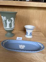 Lot display showing green vase, blue tray, and white cherub vase together on wooden surface.