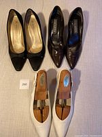 Three pairs of women's pumps displayed top-down: black suede, brown leather, and white leather slingbacks with shoe stretchers inside