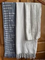 Three scarves hanging: silver shiny with stripes, white translucent with fringe, grey blue with fringe.