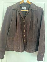 Front view of the chocolate suede leather women's jacket hanging on a wooden hanger