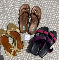 Three pairs of women's summer shoes displayed on patterned surface: Ron White wedge sandals with pink and purple ribbons, Varello green leather strappy shoes, and OkaB cognac flip flops with jewel decoration. All shoes lightly used.