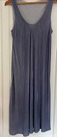 Steel blue sleeveless velvet A-line dress hanging on wooden hanger against white door.