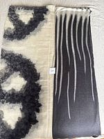 Two folded wool shawls placed side by side, one with black and grey stripes and the other with black floral circle patterns on cream.