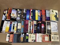 Photo showing a wide assortment of 44 books arranged in a single layer inside a box, view of spines and covers.
