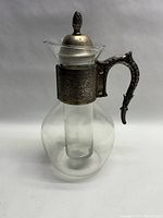Full view of antique glass pitcher with silver plate or sterling handle and intricate detailing, with glass ice insert inside.