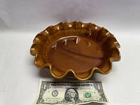 Top-down view of glazed brown pottery bowl with ruffled edges, placed next to a US dollar for size comparison