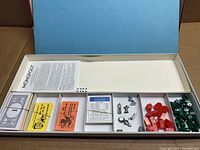 Open game box showing neatly arranged game components including cards, tokens, houses, hotels and dice.