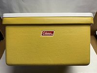 Front view of the rectangular yellow Coleman cooler with white hinged lid and Coleman logo on the front.