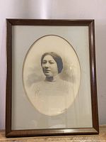 Front view of framed black and white portrait photograph of a woman in vintage clothing with wooden frame and oval matting.