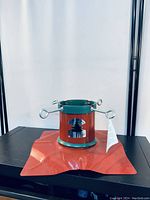 Full view of steel red Christmas tree stand with star-shaped base and green accent on the cylindrical holder with metal tightening screws.