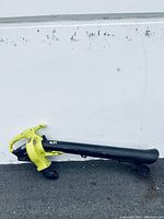 Side view of cordless leaf blower showing yellow motor housing, long black nozzle, and base wheels.